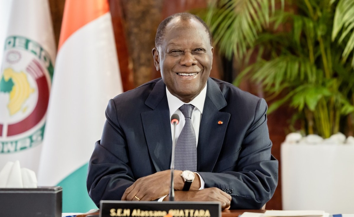 Son Excellence Alassane Ouattara, Président de la République de Côte d'Ivoire, souriant à son bureau sous les drapeaux de la République